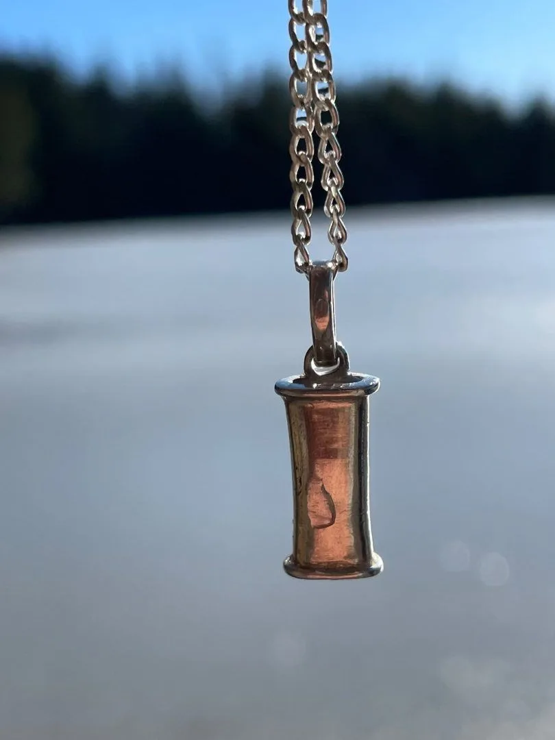 The Original Breathing Jewel pendant in sterling silver hanging against a pale lake